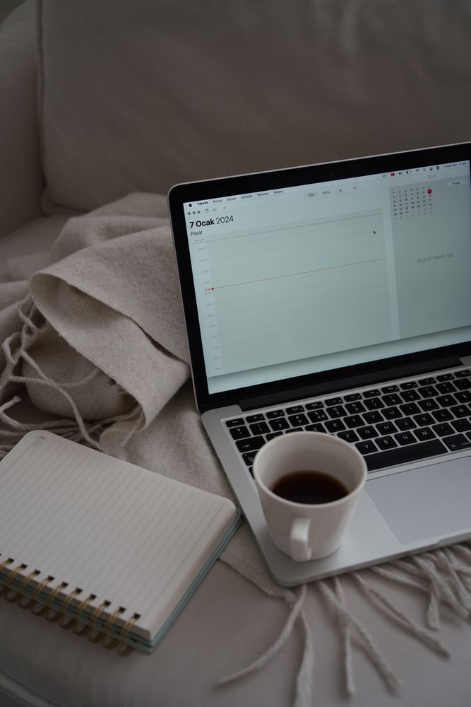 Laptop, Notizbuch und Kaffeetasse auf Sofa